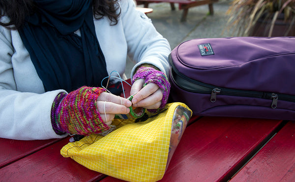 A person at an outdoor table knitting with the Luminary 15 by their side.
